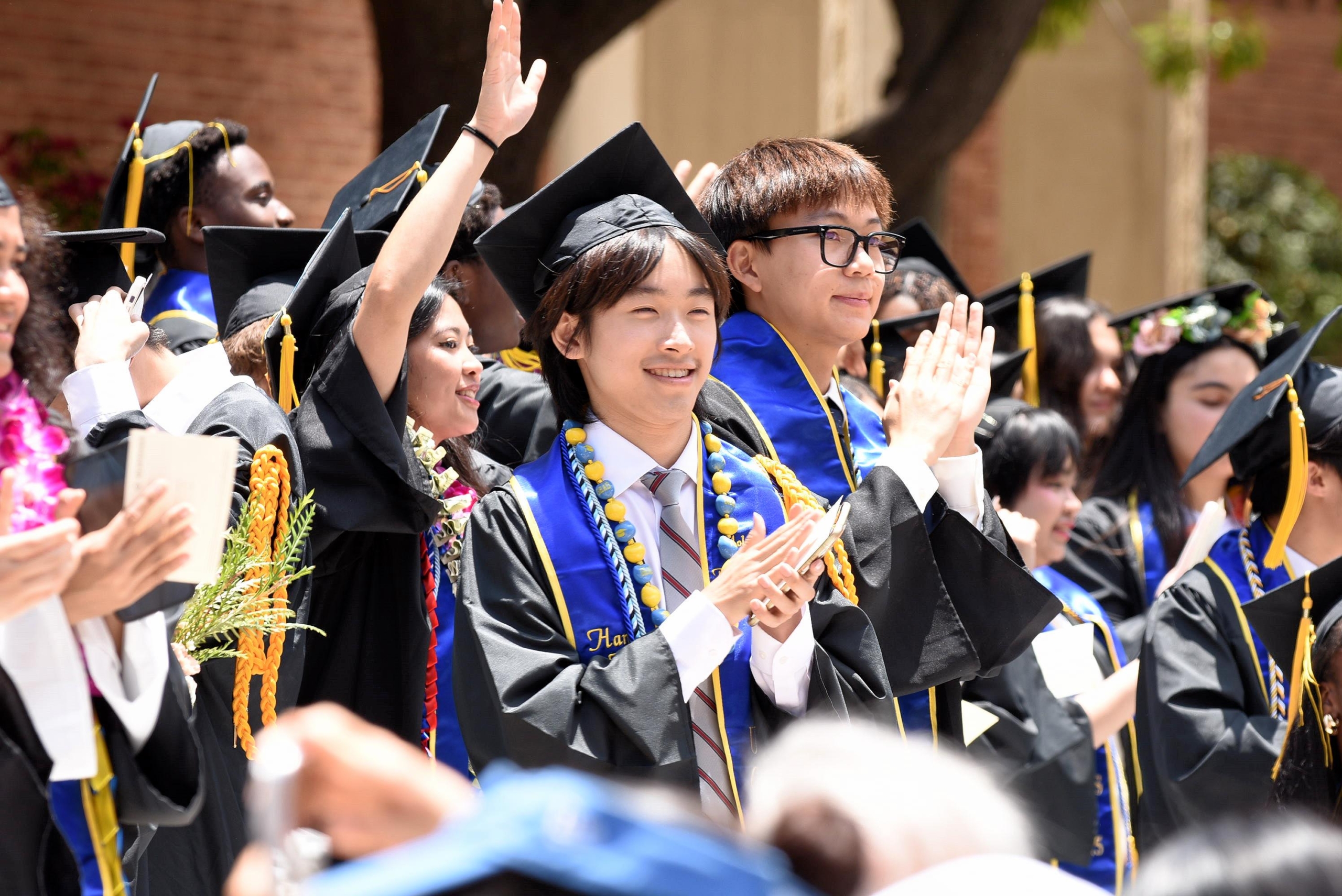 UCLA graduates in caps and gowns cheering and raising their hands at a commencement ceremony.