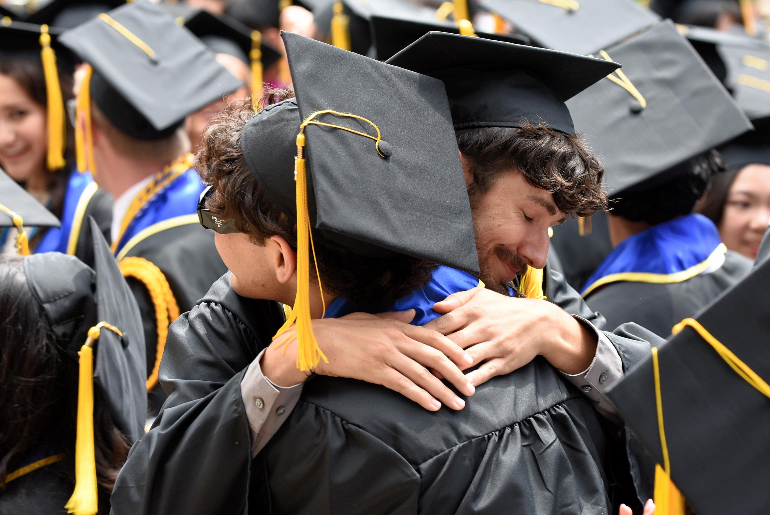 A graduate student in a cap and gown receiving a hug at a commencement ceremony.