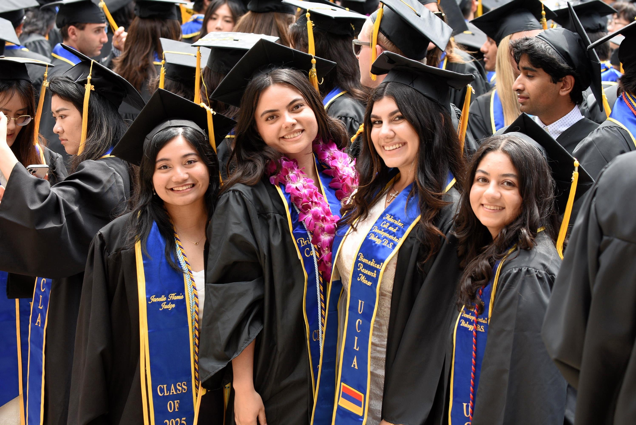 A group of UCLA graduates in black caps and gowns smiling together at a commencement ceremony.